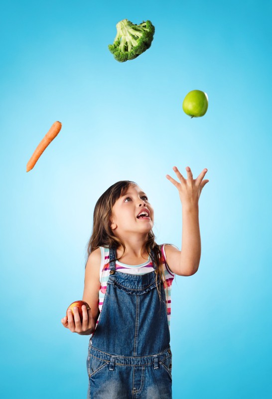 Zadowolone dziecko żonglujące warzywami.