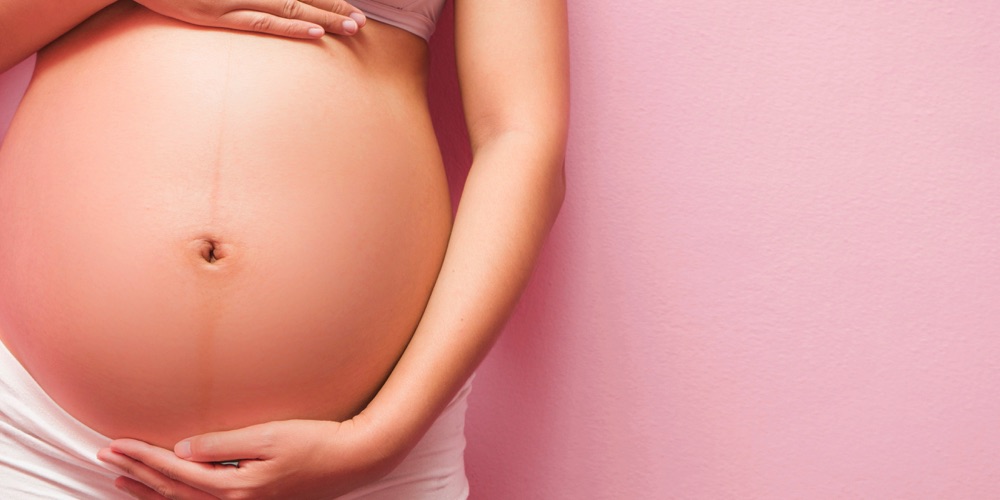 Brzuch kobiety w ciąży na różowym tle